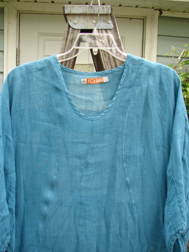 Barclay Linen High Vent Rear Tab Dress Unpainted Turquoise Size 1, displayed on a wooden stand with a plastic hanger, showcasing curved front seams, three-quarter sleeves, and an A-line shape.