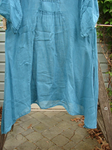 Barclay Linen High Vent Rear Tab Dress Unpainted Turquoise Size 1 hanging on a clothesline, featuring an A-line shape with varying hemlines and three-quarter sleeves, showcasing lightweight linen fabric.