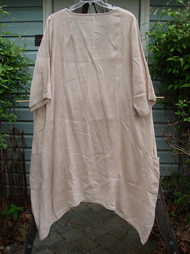Barclay Linen Drop Pocket Bell Dress Unpainted Sand Size 1 hanging on a clothesline, showcasing its elongated curved seams, three-quarter length sleeves, and A-line shape with dual drop wrap side pockets.