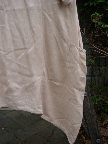Barclay Linen Drop Pocket Bell Dress Unpainted Sand Size 1 on a clothesline, showcasing its A-line shape, curved seams, and side pockets, against a backdrop of outdoor greenery.