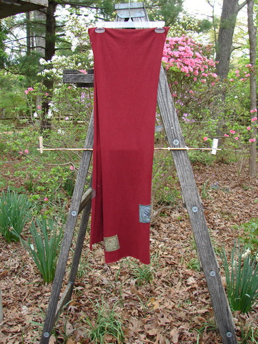 2000 PMU Patched Scarf Celtic Deep Burgundy One Size displayed on a wooden ladder outdoors, highlighting its generous length, thinner width, raw edges, and Celtic theme patches, against a backdrop of greenery and flowers.