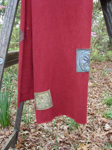 2000 PMU Patched Scarf Celtic Deep Burgundy One Size draped on a ladder, showcasing its raw edges and classic Celtic theme patches, alongside a glimpse of a green plant for visual contrast.