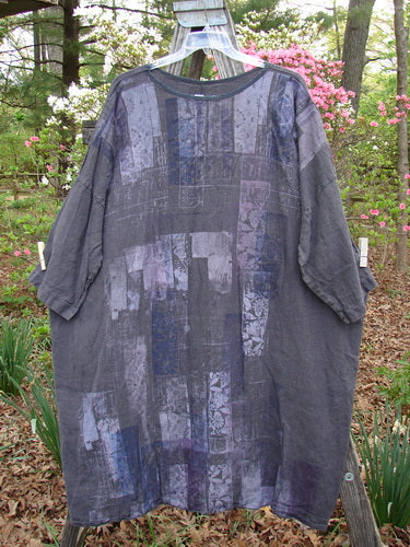 Barclay Linen Oversized Canyon Dress Floral Cityscape Black OSFA hanging on a clothesline, showcasing its rounded neckline, drop shoulders, three-quarter dolman sleeves, and floral cityscape pattern.