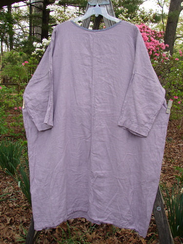 Barclay Linen Oversized Canyon Dress Floral Garden Lilac OSFA hanging on a clothesline, showcasing its rounded neckline, three-quarter dolman sleeves, and generous straight shape in an outdoor setting.