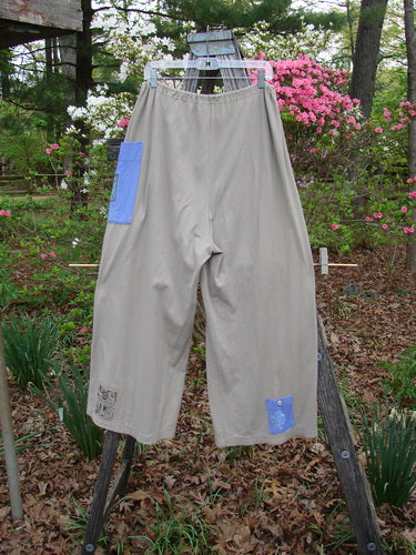 1997 Cubist Pant Top Hat Wheat Altered Size 1 hanging on a clothesline, showcasing its wide shape and multiple oversized pockets with textured buttons, made from mid-weight organic cotton.