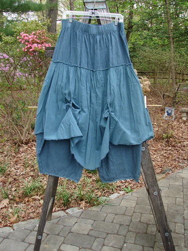 Barclay Linen Batiste Fusion Pant Skirt Unpainted Teal Size 0 displayed on a wooden stand, highlighting its dual ties, elastic waistline, and layered design against an outdoor backdrop.