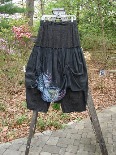 Barclay Linen Batiste Fusion Pant Skirt Galaxy Black Size 0 displayed on a wooden stand, showcasing its unique dual ties, triangular patches, and layered over piece with a billowy silhouette.