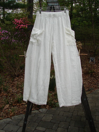 Barclay Linen Side Pocket Tie Pepper Pant Unpainted White Size 1 hangs on a clothesline, showcasing its billowy shape, full elastic waist, and exterior side pockets, enhancing its versatile style and comfort.