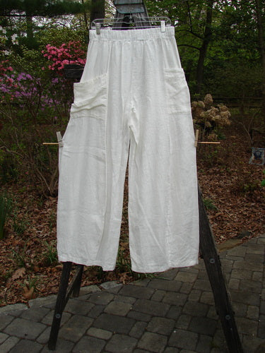 Barclay Linen Side Pocket Tie Pepper Pant Unpainted White Size 1 displayed on a wooden stand, showcasing its billowy shape, elastic waistline, and exterior side wrap pockets, perfect for versatile spring styling.