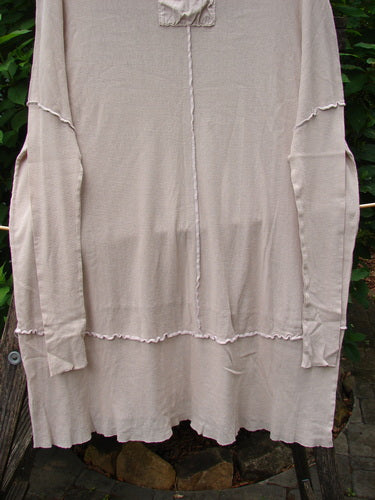 Barclay Cotton Mesh Exterior Stitch Sectional Overtop Unpainted Cloud Size 2 features a light-beige, long-sleeved knit tunic with raw-edge seams, deep neckline, and slightly flared hem, hanging outdoors.