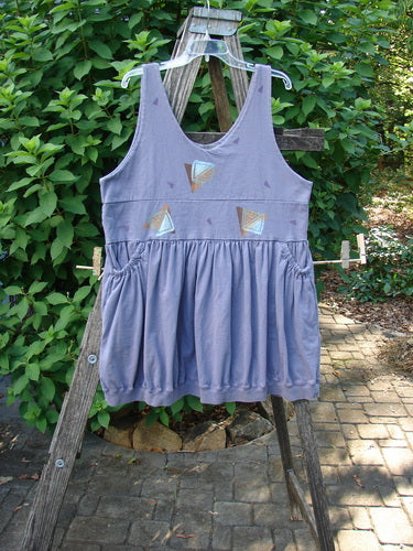 1996 Amusement Jumper Triangle Shadow Mulberry Size 1 showcases a sleeveless tunic with a gathered waist and triangular appliqués, hanging on a rustic ladder amid greenery, embodying vintage charm.