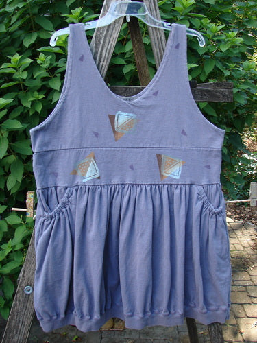 1996 Amusement Jumper Triangle Shadow Mulberry Size 1: A sleeveless, scoop-neck tunic with geometric appliqués and ruched side pockets. Features an empire waist and gathered skirt, hanging against a wooden trellis.