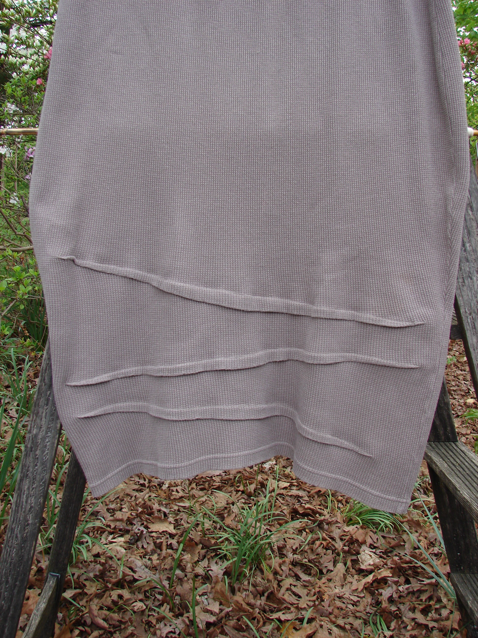 Barclay Thermal Awen Skirt Unpainted Stone Size 0 displayed draped over a wooden ladder, showcasing its unique bell shape and textured diagonal hemline.
