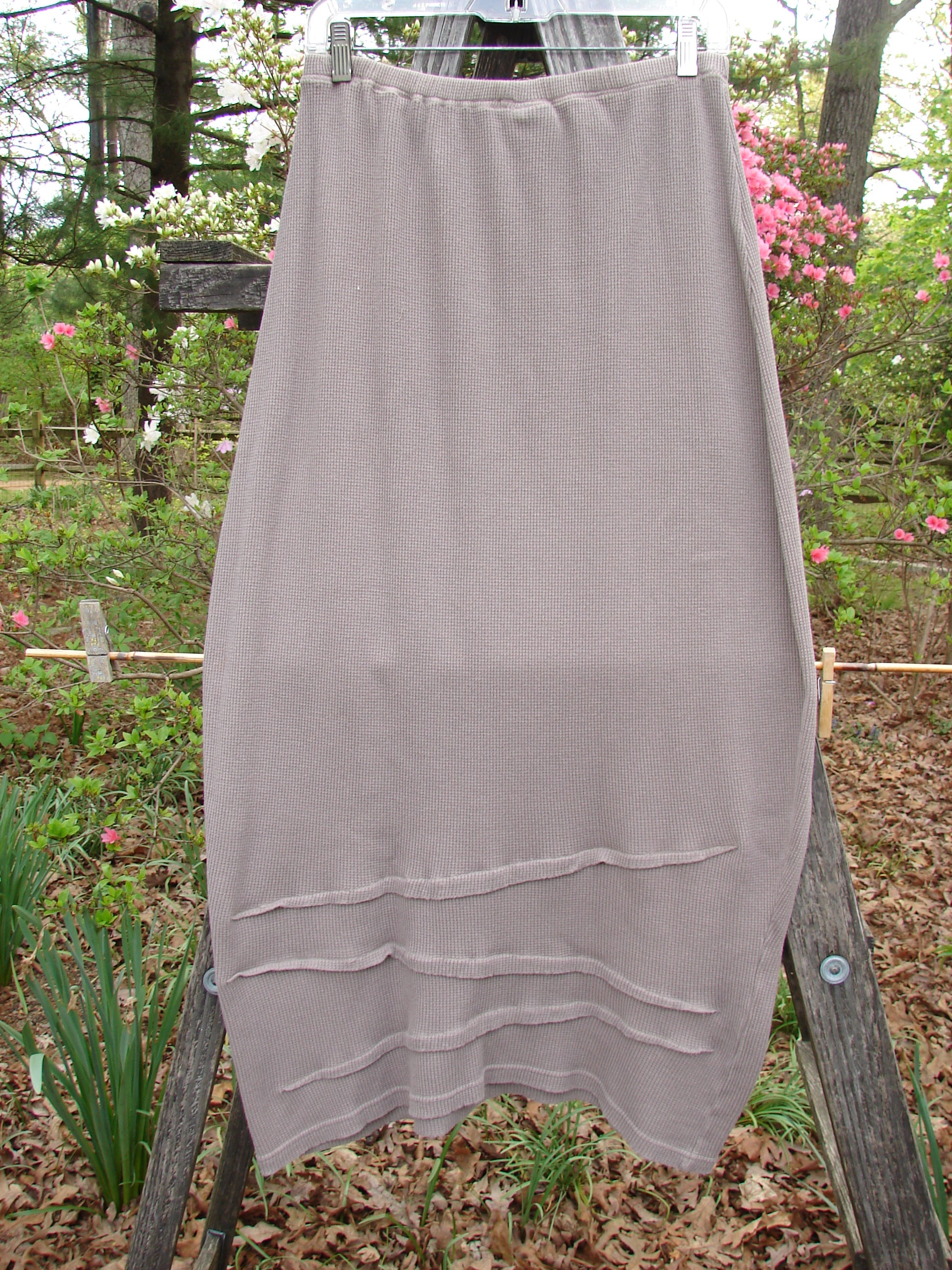 Barclay Thermal Awen Skirt Unpainted Stone Size 0 draped on a wooden ladder, showcasing its unique bell shape, textured diagonal hemline, and full elastic waistband, highlighting its vintage-inspired design.