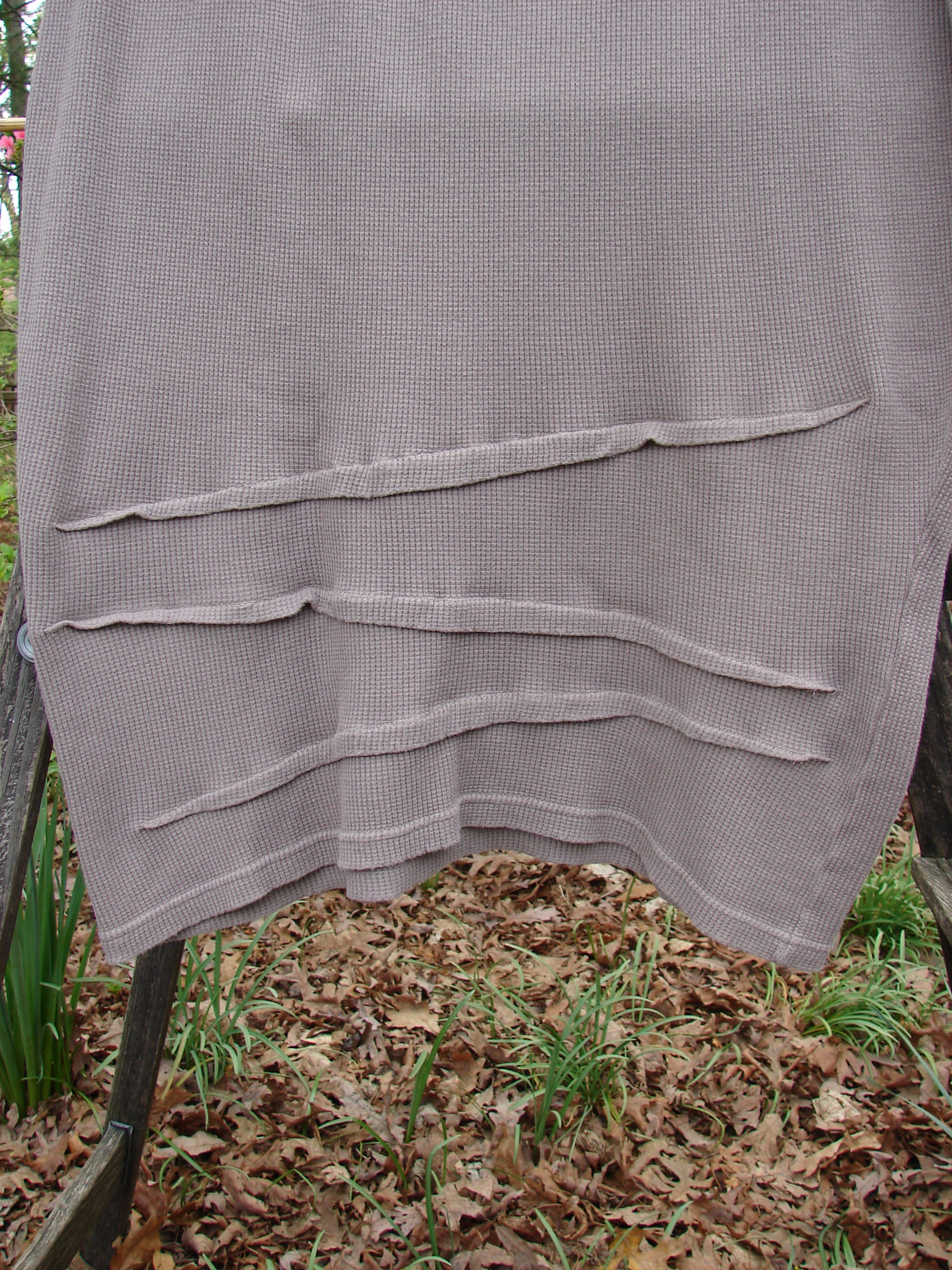 Barclay Thermal Awen Skirt Unpainted Stone Size 0 displayed draped over a wooden railing, highlighting its textured, uniquely shaped design with a full elastic waistband and bell-shaped lower taper.