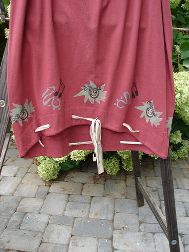 1992 Buttonloop Skirt Pomegranate Music OSFA: red cotton skirt with white laces draped on a chair, featuring a drawcord waist, bell shape, and music-themed art.