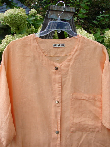 Barclay Linen Vented Crop Pocket Top Unpainted Sherbet Size 2 displayed on a wooden stand, featuring a softer V neckline, widening crop shape, side vents, shell-like buttons, and an oversized breast pocket.