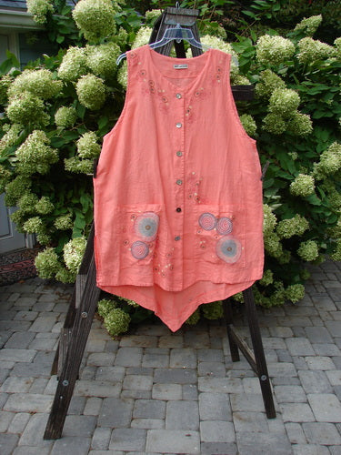 Barclay Linen Katy Vest Circle Spin Tangerine Size 2, displayed on a wooden stand, features pearly buttons, a varying hemline, oval neckline, exterior drop pockets, and deeper arm openings.