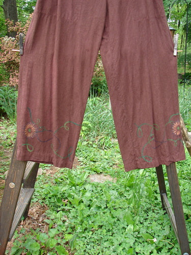Barclay Tencel Collar Drawstring Studio Duo Spin Flower Sepia Size 1: A pair of pants on a clothesline with a wooden fence post and a green plant.