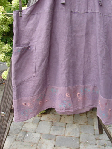 Barclay Linen Patterson Flutter Apron Jumper Butterfly Dusty Plum Size 2 displayed hanging on a ladder, showcasing its mega sectional panels, flutter hem, and exterior side pockets.
