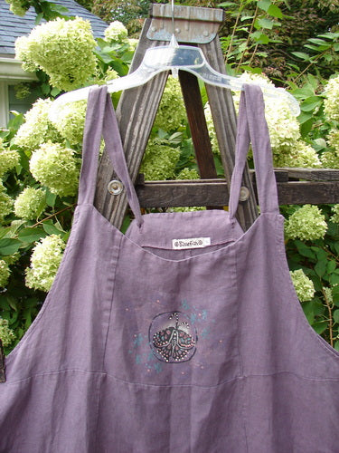 Barclay Linen Patterson Flutter Apron Jumper Butterfly Dusty Plum Size 2 displayed on a swing, showcasing adjustable shoulder straps, mega sectional panels, and two exterior pockets with butterfly-themed paint accents.