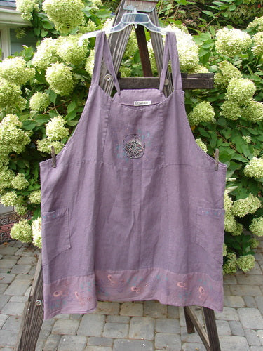 Barclay Linen Patterson Flutter Apron Jumper Butterfly Dusty Plum Size 2 displayed on a wooden ladder, showcasing its adjustable shoulder straps, sectional panels, and exterior side pockets.