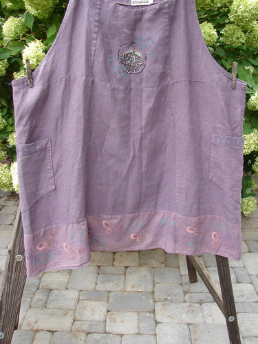 Barclay Linen Patterson Flutter Apron Jumper Butterfly Dusty Plum Size 2 hanging on a clothes rack, showcasing sectional panels, batiste flutter hem, butterfly theme, and adjustable shoulder straps.