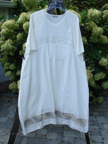 Barclay Linen Cotton Sleeve Banded Hem Pleat Dress Curl Fern White Size 2, hanging on a clothesline, showcasing its pleated design and three-quarter length sleeves, with visible plant elements in the background.