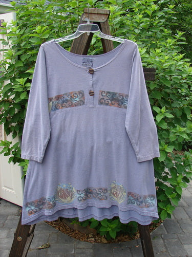 1993 Sparrow Dress Continuous Celtic Periwinkle OSFA displayed on a clothes rack, showcasing its patterned cotton jersey fabric, downward yoked waist seam, wooden button closure, and varying hemline with vintage banded design.