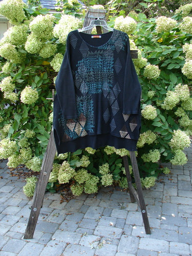 Barclay Thermal Shirttail Top Continuous Mosaic Black Size 1 displayed on a rack, showcasing its A-lined shape, shirttail rear hemline, and mosaic-themed front design with longer sleeves.