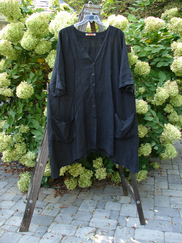 Barclay Linen Double Tie Back Jacket Unpainted Black Size 1 displayed on a wooden rack, featuring a deep V-neckline, A-line sweep, exterior vertical stitching, and front drop pockets.