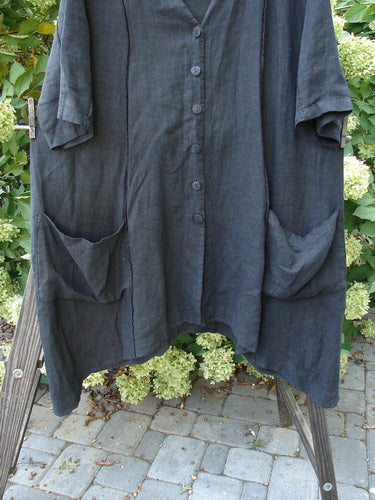 Barclay Linen Double Tie Back Jacket in Black, displayed on a clothes rack, featuring a deep V neckline, A-line sweep, vertical stitchery, front drop pockets, and varying hemline.