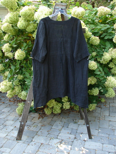 Barclay Linen Double Tie Back Jacket Unpainted Black Size 1 hanging on a rack, showcasing deep V neckline, A-line sweep, vertical stitching, front pockets, and varying hemline.