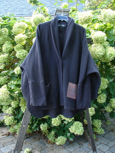 Barclay Patched Celtic Moss Deco Coat Farmhouse Brum OSFA displayed outdoors on a swing, showcasing its dense cotton fleece, oversized vintage button, dolman shoulders, and deep V neckline with a stand-up rear collar.