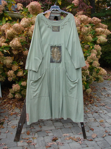 1995 Farmer Jen Dress Fall Leaves Dinette Green Size 2: A long, medium-weight cotton jersey dress with cozy sleeves, deep pockets, and fall leaf patterns, hanging on a rack.