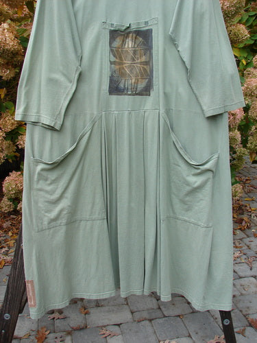 1995 Farmer Jen Dress Fall Leaves Dinette Green Size 2, featuring a deep rounded neckline, cozy long sleeves, stacked and tunnel pockets, and center lower pleats, shown in medium-weight cotton jersey.