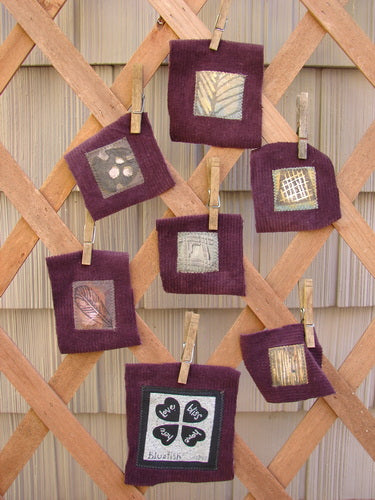 The PMU 1999 Fall Woods Patch Set Total 7 mounted on deep burgundy cotton corduroy, displayed in a group on a wooden lattice, showcasing intricate fabric squares and designs.