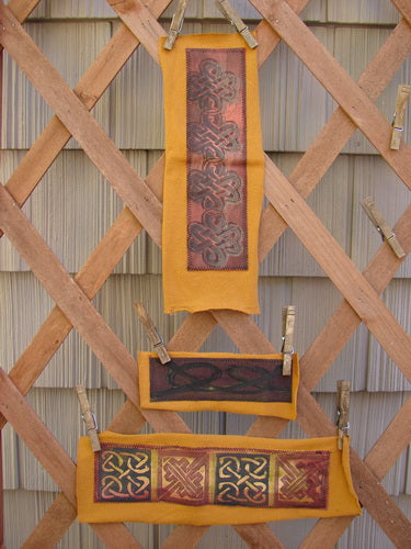 The PMU 2000 Winter Celtic Knot Patch Set Total 3, displayed on a wooden lattice, showcasing intricate fabric pieces in a close-up view, highlighting the detailed craftsmanship.