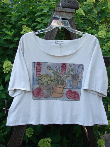 Barclay Crop Tee Top Bountiful Cacti Natural Altered Size 1 features a painting of potted cacti on a white shirt, with a cropped hem, wider short sleeves, and a rounded neckline.