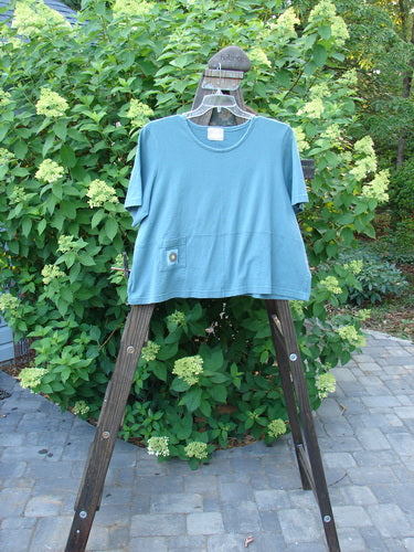 2000 Pocket Crop Tee Top Earth Day Blue Mineral Size 2 displayed on a wooden rack, highlighting its sweet swingy hemline and double-layered front pocket.