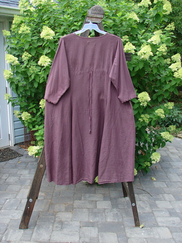 Barclay Linen Cotton Sleeve Upper Pocket Dress Unpainted Red Plum Size 2 hanging on a rack, showcasing its A-line flair, rounded neckline, and three-quarter length sleeves with a cotton lettuce edge.