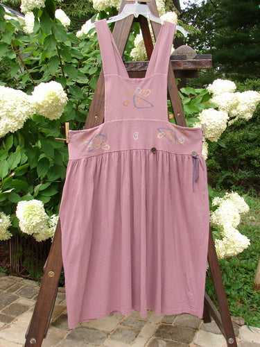 1996 Souvenir Jumper Abstract Path Petunia Size OSFA displayed on a wooden stand, featuring a full gathered skirt, criss-cross back, and painted bib, with missing front pocket.
