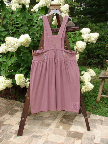 1996 Souvenir Jumper Abstract Path Petunia Size OSFA displayed on a wooden rack, showcasing its organic cotton fabric, two-button front accent, gathered skirt, and crisscross back design.