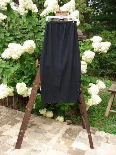 1993 Tie Skirt Unpainted Black Size 1 displayed on a wooden rack, highlighting its full elastic waistline, velvet side ties, and slightly pegged, vented design.