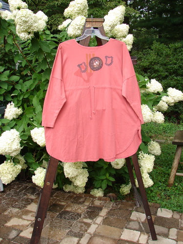 1996 Long Sleeved Pop Top Boulder City Oriole OSFA with floral design, scooped neckline, drop shoulders, exterior front pocket with ceramic button, rear drawcord, and rounded hemline on a hanger.