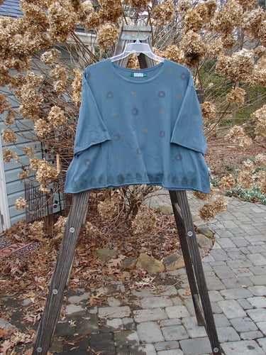 Barclay Crop A Lined Tee Top Continuous Pinwheel Puddle Size 2 displayed on a wooden stand, showcasing its short sleeves, wide boxy shape, rolled neckline, and sweet rolled edgings.