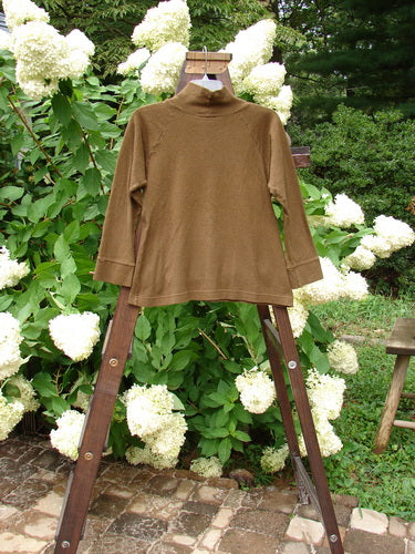2000 Wool Funnel Neck Raglan Top Unpainted Pebble Smaller Size 1: a brown shirt on a wooden stand, with a relaxed half-height turtleneck and a front center cargo pocket.
