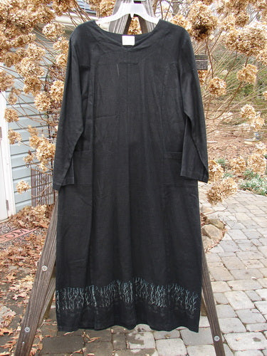 2000 Ringlet Dress Grass Row Black Size 1: A black dress with two front oversized pockets and a top rounded V-shaped neckline, displayed on a wooden rack.