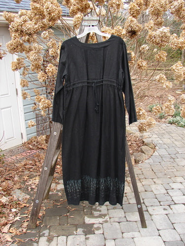 2000 Ringlet Dress Grass Row Black Size 1 displayed on a wooden ladder, showcasing its oversized pockets, V-shaped neckline, and double drawcord back.