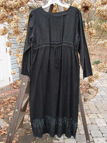 2000 Ringlet Dress Grass Row Black Size 1 displayed on a wooden ladder, showcasing a daisy-themed hem, oversized pockets, and a rounded V-shaped neckline.